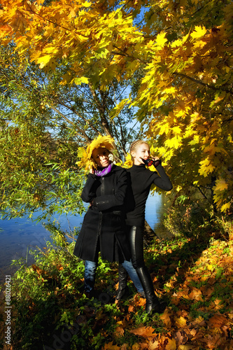 Two young beautiful woman in autumn park by the river