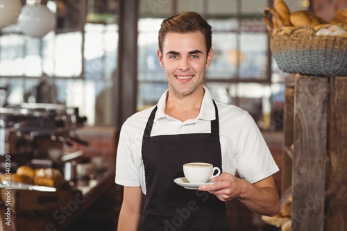 Smiling barista offering cup of coffee to camera