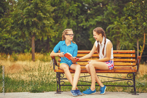 Best friends are discussing book sitting on bench.