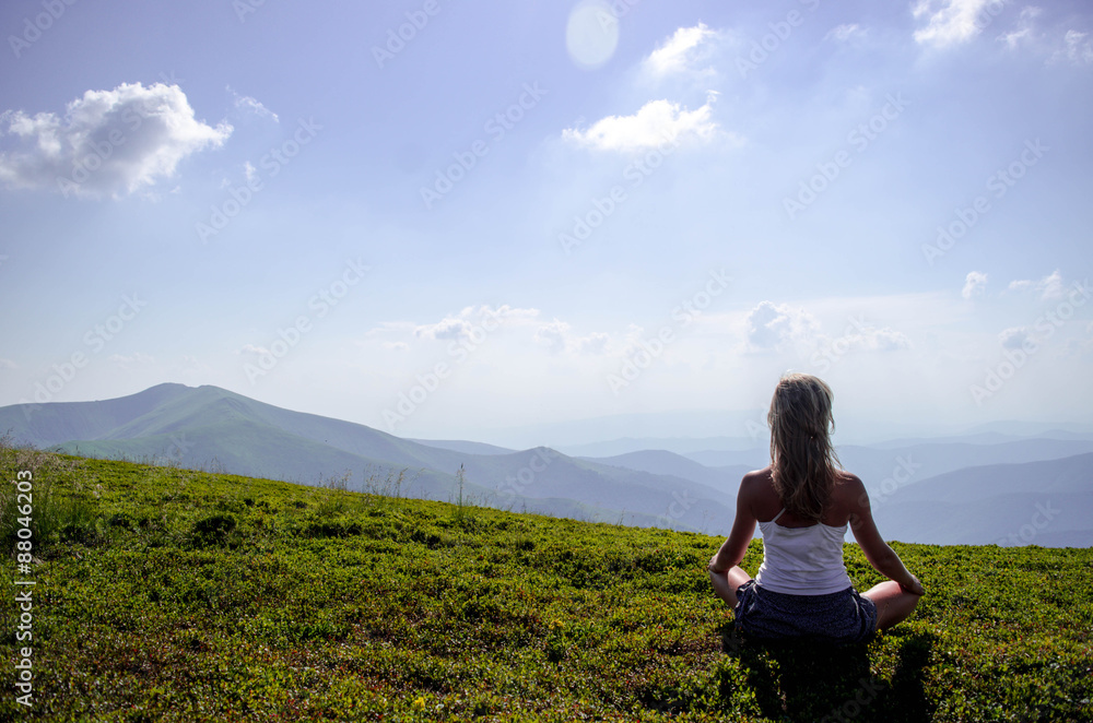 Young blonde woman meditating at the mountain peak