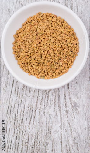Fenugreek seeds in white bowl over wooden background