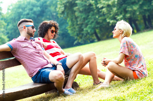 Three friends sitting on a bench in a meadow and talking