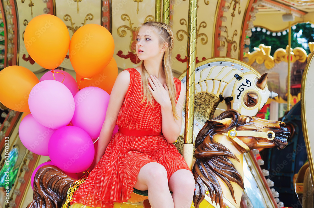 Blonde teenager having fun in the park riding a carousel