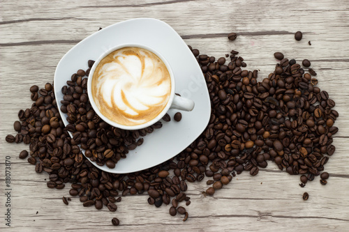 Cappuccino in weißer Tasse auf Holzuntergrund mit Kaffeebohnen