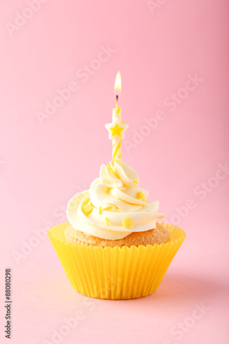 Tasty cupcake with candle on pink background
