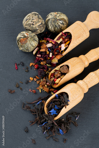 assortment of tea in scoops on black stone background