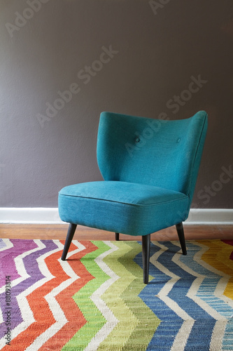 Single teal blue armchair and colorful chevron pattern rug interior