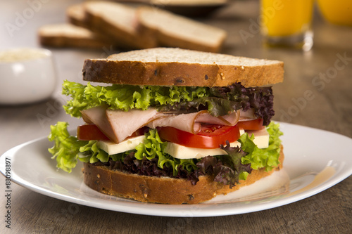 Sandwich on a white plate with turkey breast, tomato and lettuce.