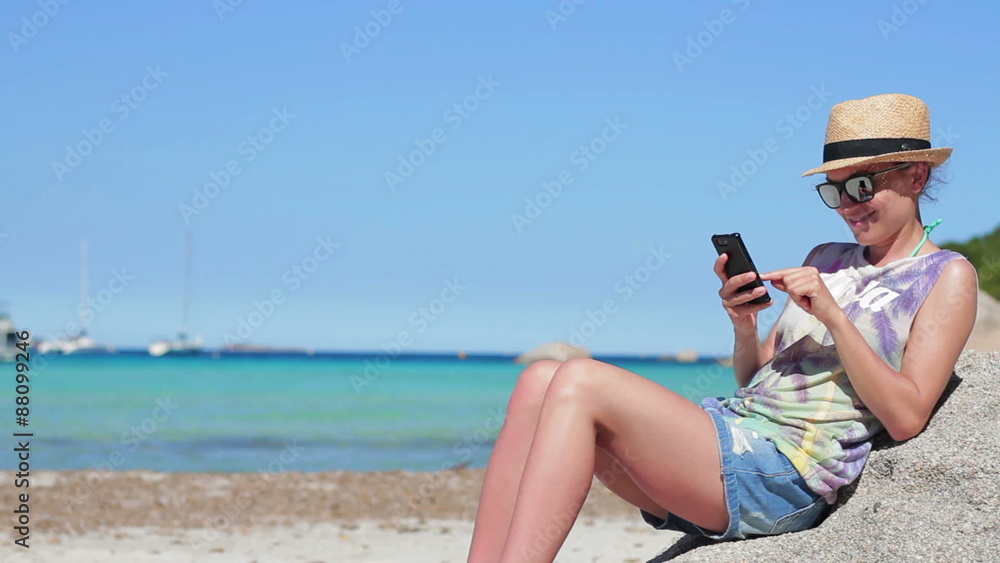 Young woman reading or writing sms on her mobile smartphone by turquoise sea Young woman reading or writing sms on her mobile smartphone by turquoise sea