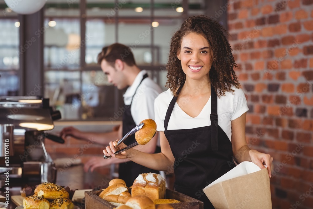 Smiling waitress putting bread roll in paper bag