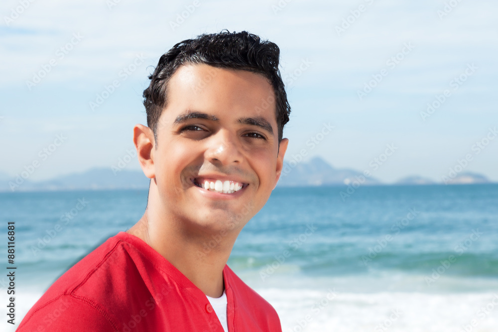 Lachender Latino im roten Shirt am Strand