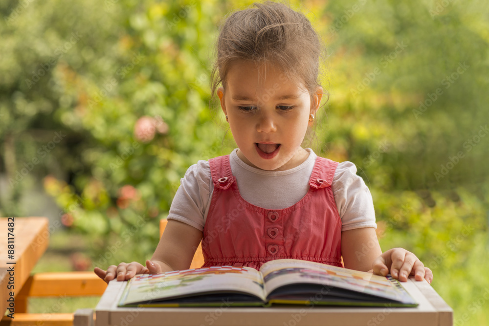 Outdoor portrait of an adorable young little girl reading a book in the garden Outdoor portrait of an adorable young little girl reading a book in the garden