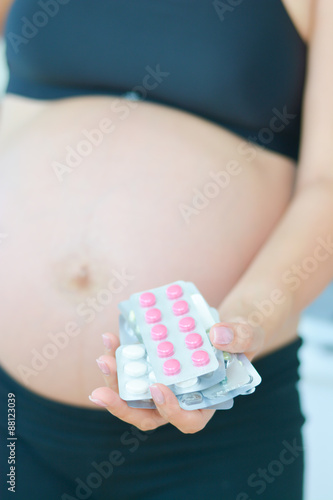 Pregnant woman holding drugs, pills and capsules in blister packs in her hand