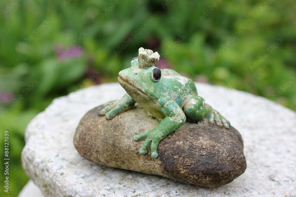 Waiting weathered stone frog statue waiting on a stone to be kissed in the garden, seen from birds eyes view looking up. Character from a Russian fairytale. Black eyes. Blurry green background. Waiting weathered stone frog statue waiting on a stone to be kissed in the garden, seen from birds eyes view looking up. Character from a Russian fairytale. Black eyes. Blurry green background.