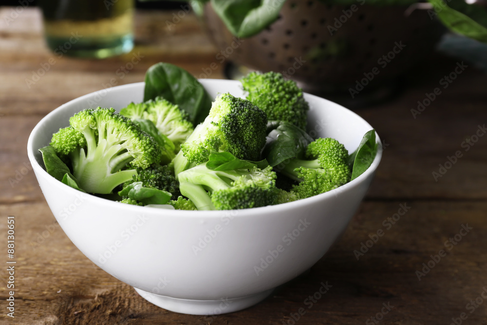 Fresh broccoli with spinach in bowl on wooden table close up Fresh broccoli with spinach in bowl on wooden table close up