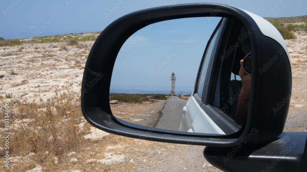 Cap de Babaria lighthouse seen through the car's rear-view mirror