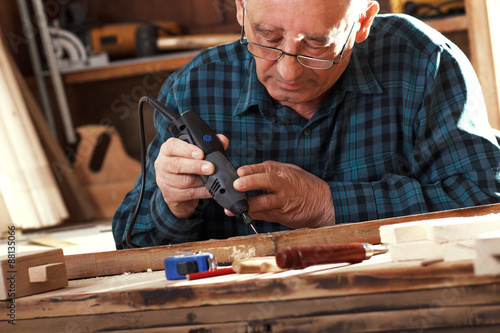 Konstfotografi Senior carpenter carving wood with engraver tool