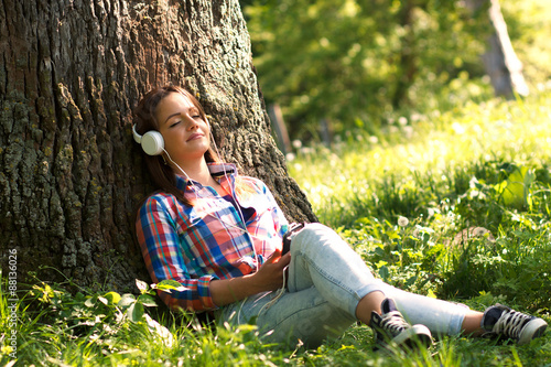 Young woman sitting in the park and listening the music from a smart phone photo