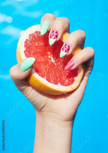 Hands close up of young woman with watermelon manicure holding slice of grapefruit summer manicure nails art and food concept 