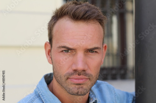 Horizontal close-up portrait of a serious confident gorgeous male model with a city stylish background