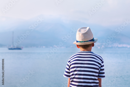 child in hat looking at sea and ship