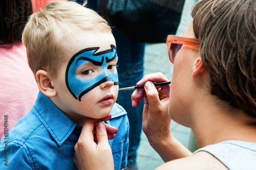 Woman painting face of kid outdoors