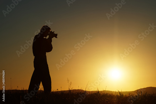 Silhouette of the photographer on a grassy horizon at sunset. Wooded mountains in the background.