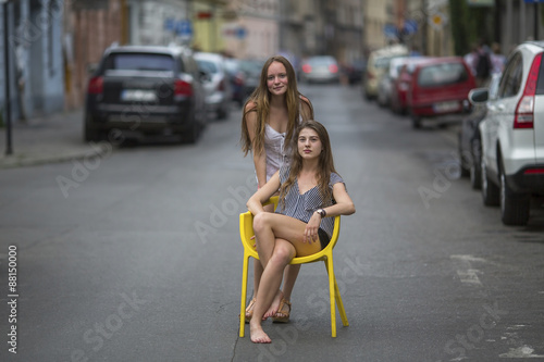 Cute adolescent girls sitting on a chair in the middle of the streets of the old town.