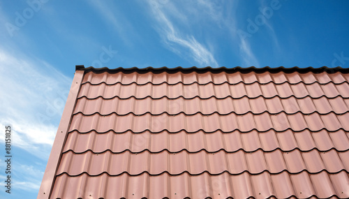 Roof of a country house covered with brown metal tile closeup against blue sky with white clouds