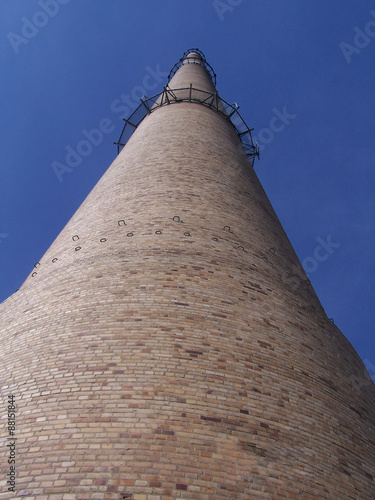 Schornstein/ein hoher Schornstein vor einem wolkenlosen blauem Himmel, Ziegelbau, Blick aus der Froschperspektive photo