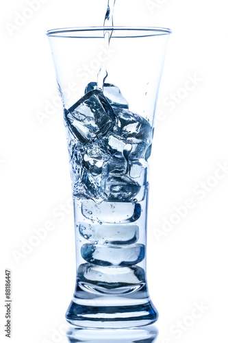 pouring water in an elegant tall glass with ice and water drops on white background