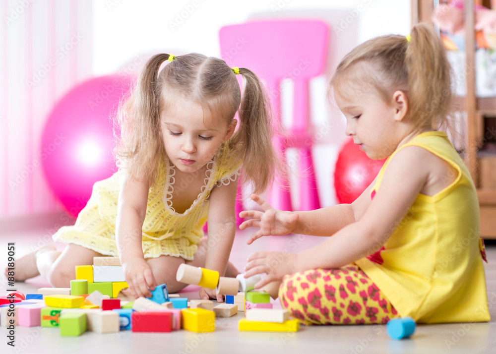 Children playing with wooden blocks sitting on the floor in room Children playing with wooden blocks sitting on the floor in room