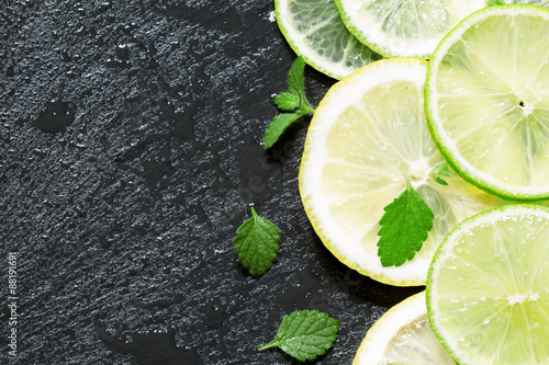 Sliced lemon, lime and mint leaves on a dark background, top vie