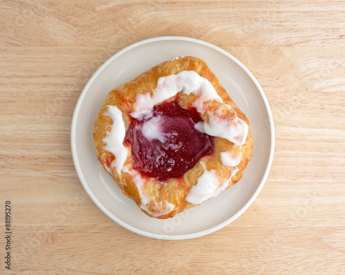 Raspberry danish on a small plate atop wood table top view