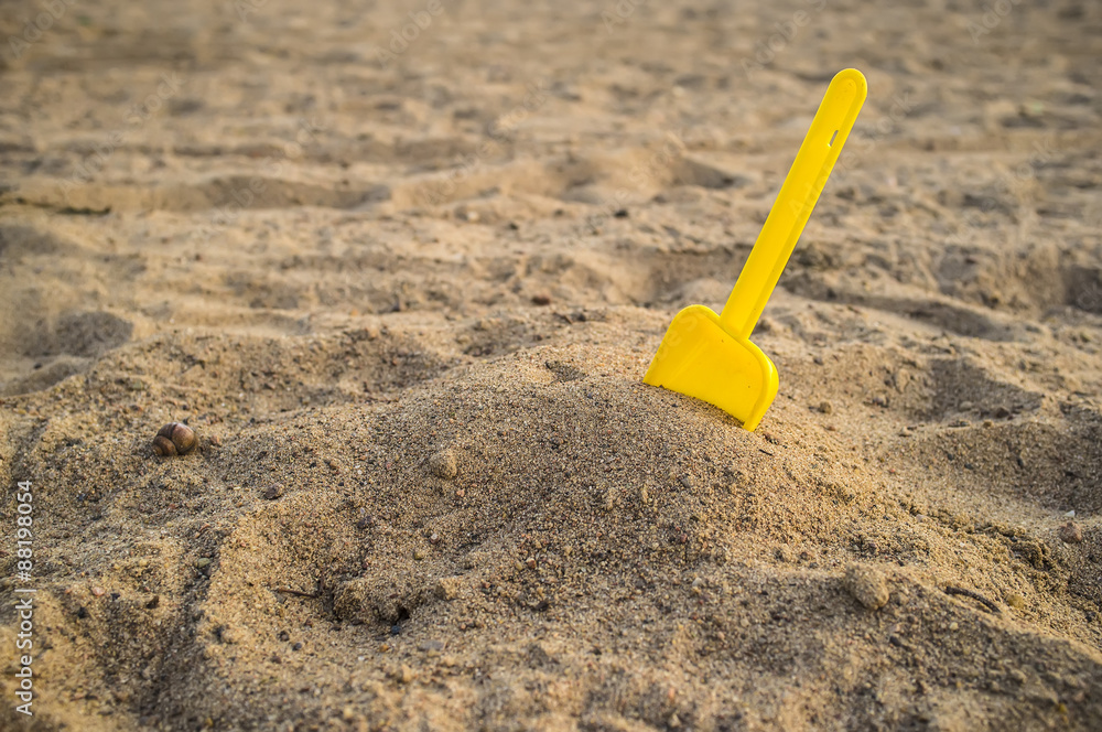 Children's yellow shovel stuck in a pile of sand on the beach Children's yellow shovel stuck in a pile of sand on the beach