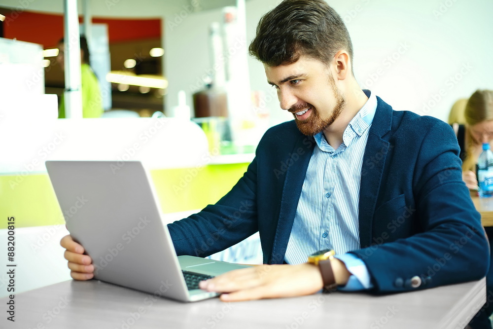 Young fashion smiling hipster man in the city cafe during lunch time with notebook in suit Young fashion smiling hipster man in the city cafe during lunch time with notebook in suit