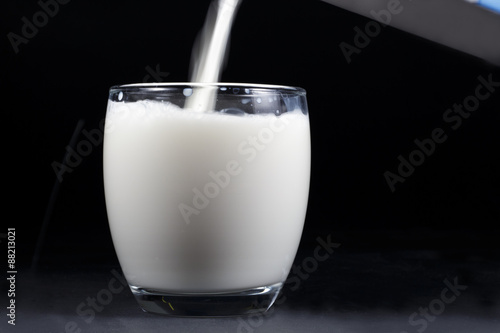 A jet of cow milk falling into a crystal glass almost full, isolated on black background