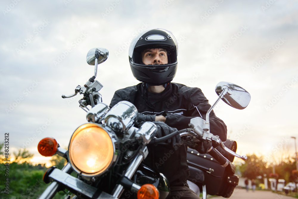 Naklejka premium Biker in helmet driving motorcycle on sunset.