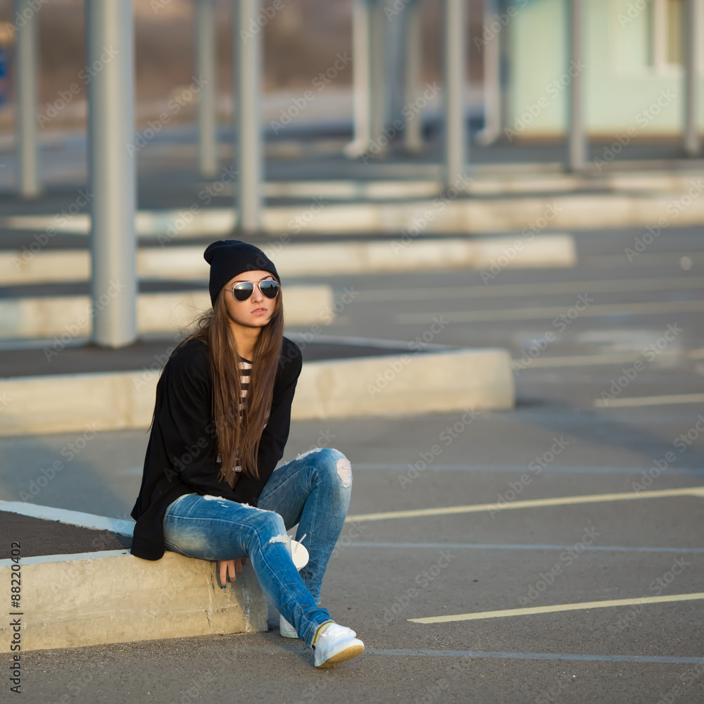 Outdoor fashion closeup portrait of nice pretty young hipster woman posing in sneakers and sunglasses sitting on the curb with a drink at sunset. Outdoor fashion closeup portrait of nice pretty young hipster woman posing in sneakers and sunglasses sitting on the curb with a drink at sunset.