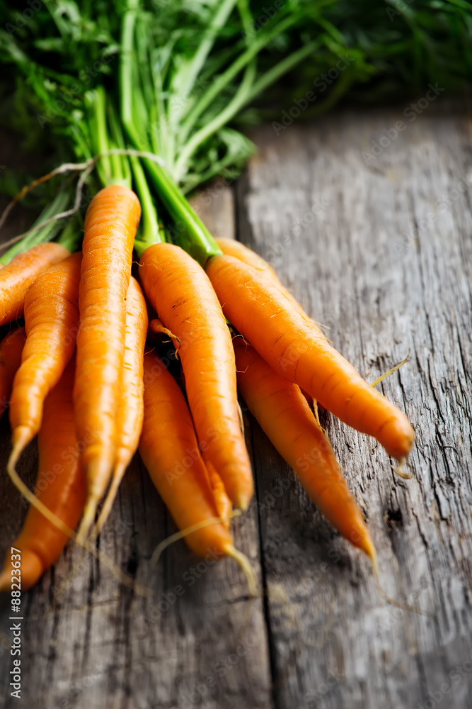 Raw carrot with green leaves on wooden background Raw carrot with green leaves on wooden background