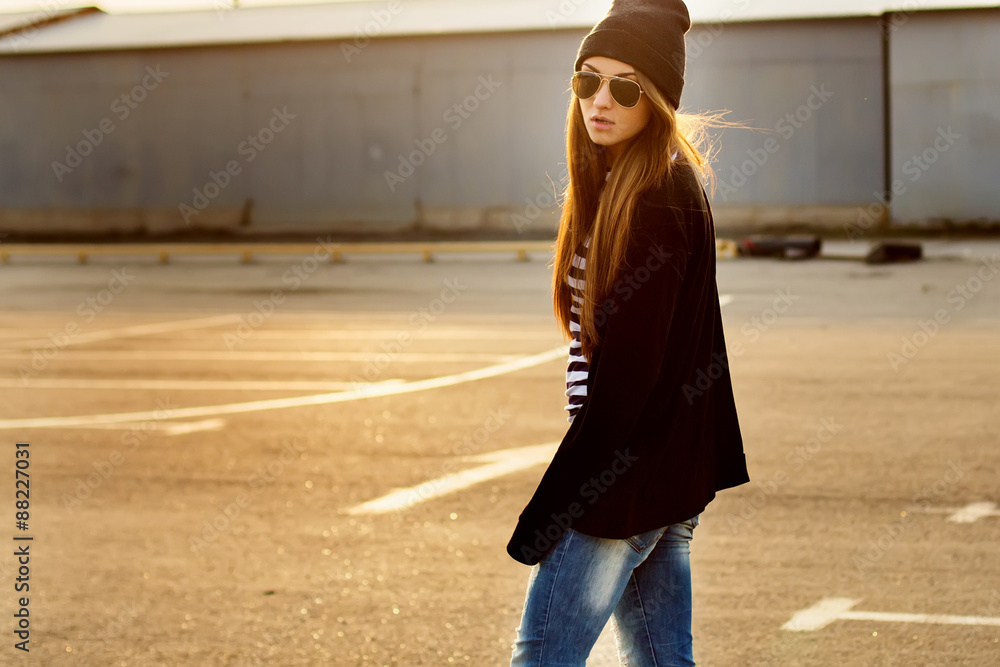 Fototapeta premium Outdoor fashion closeup portrait of nice pretty young hipster woman posing in sunglasses at sunset walks along the streets of the city.