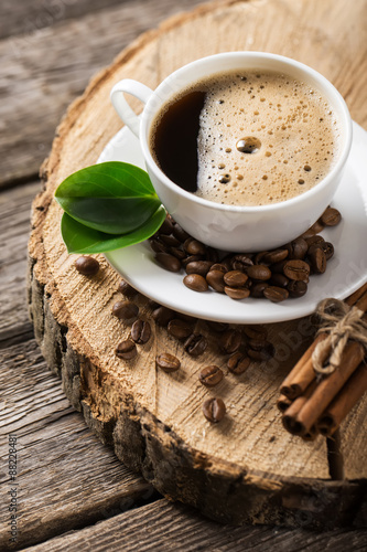 Close-up of coffee cup with roasted coffee beans on wooden background.