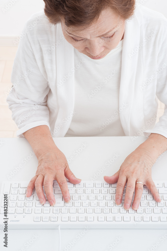 Fototapeta premium パソコンのキーボードを使っている高齢者の女性
