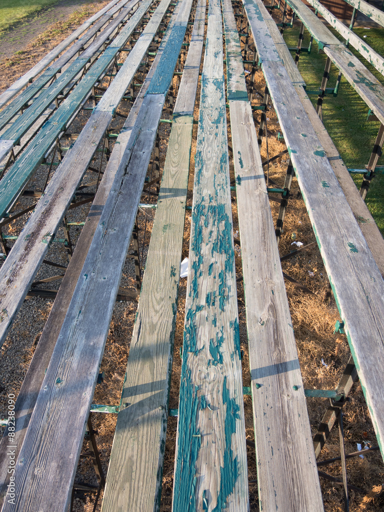 The old wooden bleachers offer peeling paint on the seats to the spectators at a football field. The old wooden bleachers offer peeling paint on the seats to the spectators at a football field.