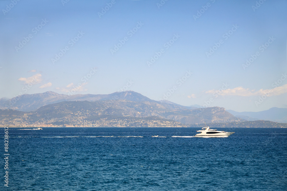 Seascape with mountains at the background and white yacht sailing in sea waters 