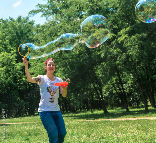 Happy young girl has fun with bubbles in a summer day in a park. She is smiling. She has tattoo and a vintage style with bandana and old school t-shirt 
