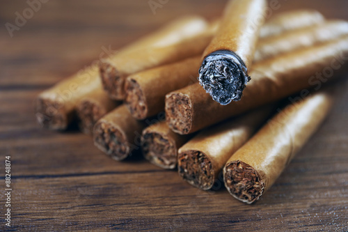 Cigars and burnt one with ash on wooden table, closeup