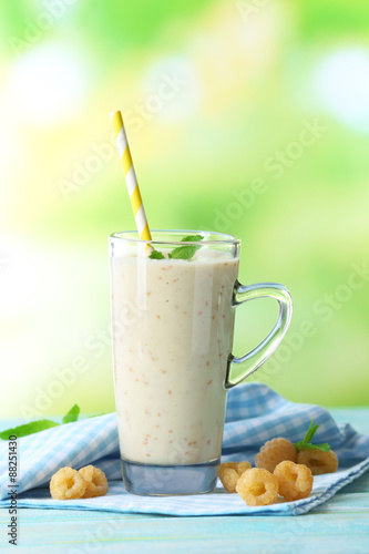 Glass of raspberry smoothie on wooden table on light blurred background