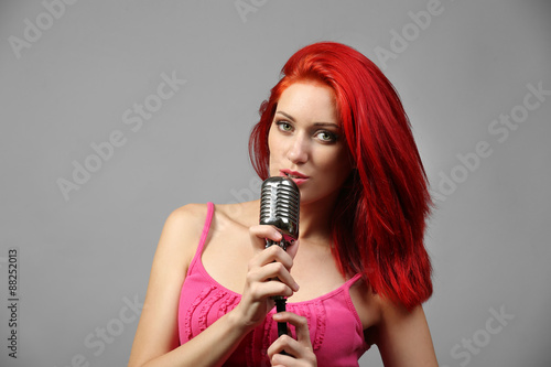 Beautiful young woman with microphone on gray background