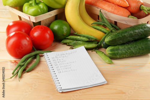 Shopping list wit fresh vegetables and fruits on wooden table, closeup